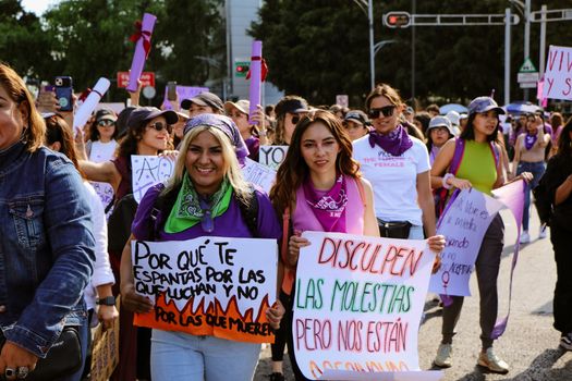 Groupe de femmes en marche avec des pancartes et des foulards violets, exprimant leur solidarité féministe.